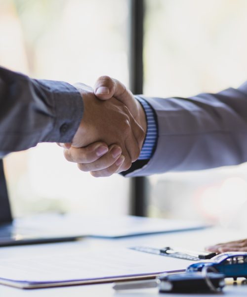 Businessmen shaking hands after signing a car sale with a car salesman.